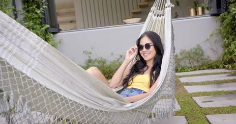 Woman relaxing in backyard hammock on summer day