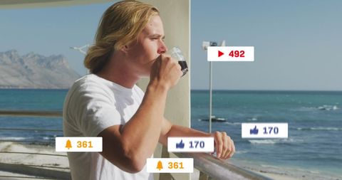 Man drinking coffee by seaside with floating social media icons