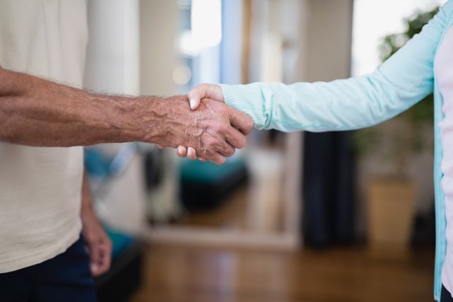 Senior patient shaking hands with female therapist in hospital ward. Ideal for illustrating themes of healthcare, trust, patient-therapist relationships, medical support, and elderly care. Useful for medical websites, healthcare brochures, and wellness blogs.