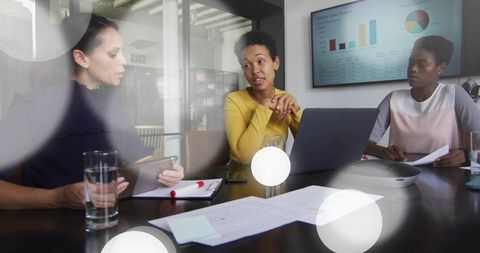 Woman leading boardroom meeting wearing yellow sweater presenting sales data on laptop