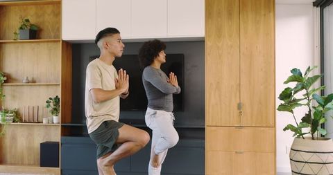 Friends practicing yoga tree pose at home emphasizing trust and flexibility