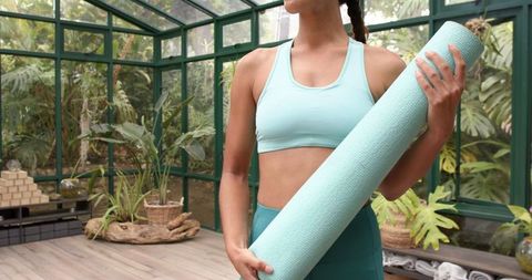 Woman in Activewear Holding Yoga Mat in Tranquil Glasshouse