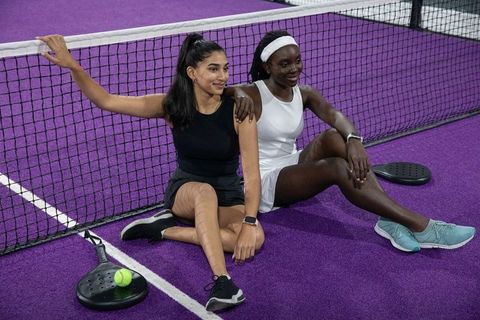 Female teammates relaxing and smiling at net on purple paddle court after training