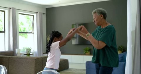 African american grandmother dancing with granddaughter in bright cozy living room