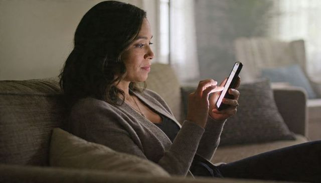 Woman using smartphone on sofa at home, relaxing in cozy living room with soft light