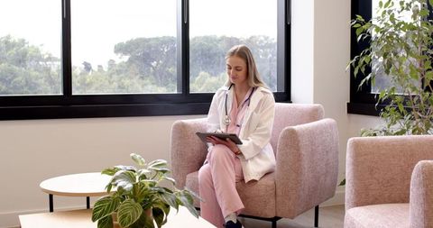 Female doctor reviewing tablet in modern clinic waiting room with plants and natural light