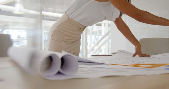 An architect reviews blueprints at an office desk. Precision and attention to detail are key in her work environment.