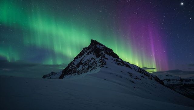 Aurora Borealis Stretching Over Snowy Mountain Peak Under Starry Polar Night Sky