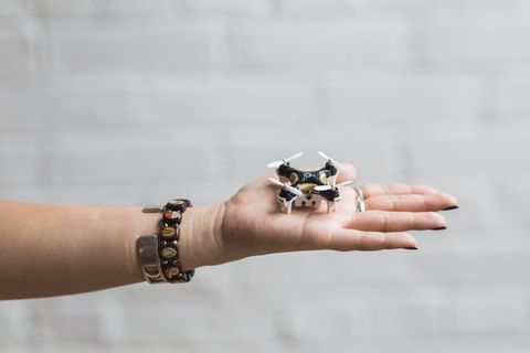 Hand displaying tiny drone against white brick background