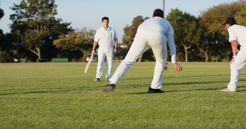 Evening cricket match with bowler delivering ball and batsman ready on sunlit grassy pitch