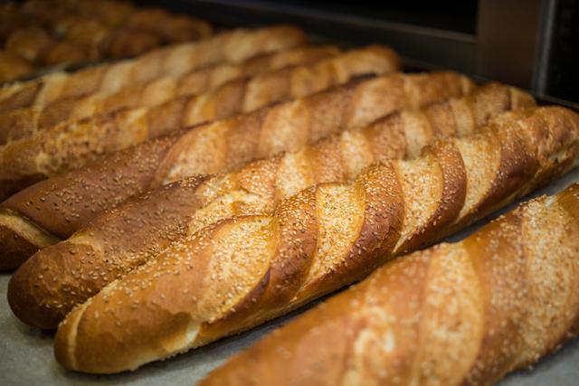 Close-up of freshly baked French baguettes with sesame seeds on a tray. Perfect for bakery promotions, food blogs, culinary websites, and advertisements for bread and pastry products.