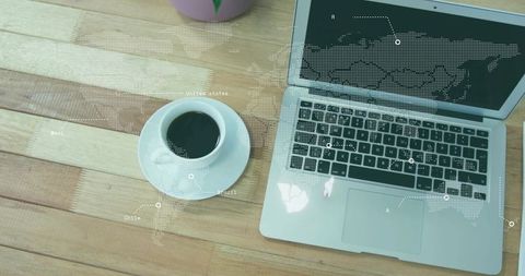 Silver laptop and coffee on wooden desk with dotted world map overlay for remote work
