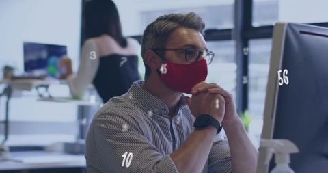 Thoughtful office worker wearing red face mask focusing on analytics at modern workspace