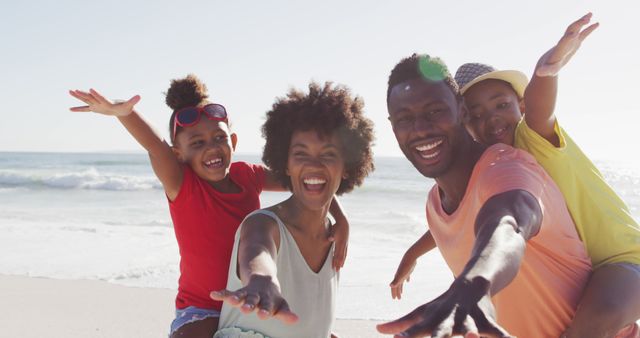 Portrait of smiling african american family embracing on sunny beach. healthy, active family beach holiday.