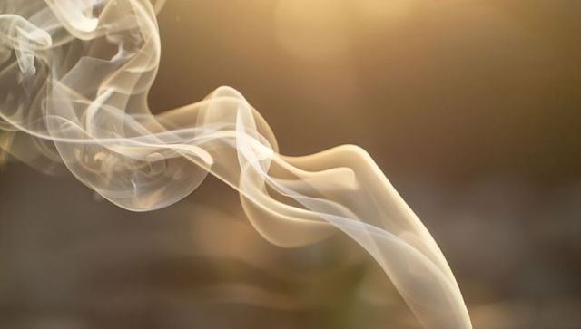 Golden backlit smoke trail flowing in graceful ribbons over soft gradient background