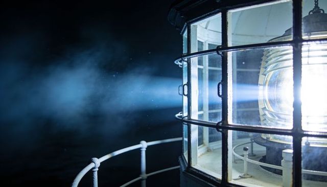 Lighthouse beacon emitting bright fresnel lens beam across misty coastal night lantern room