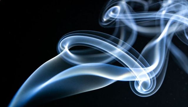 Swirling blue smoke ribbons drifting over black backdrop, ethereal abstract vapor