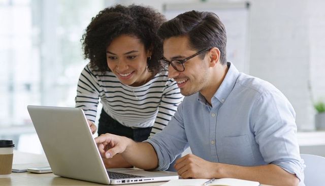 Smiling professionals collaborating on laptop, sharing ideas in bright modern office