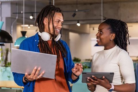 African american woman and male coworker collaborating with laptop and tablet in modern open office