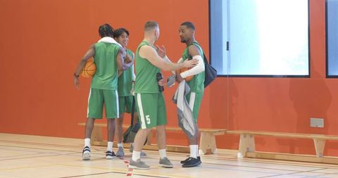 Diverse basketball teammates greeting, gathering balls and heading off court in gym