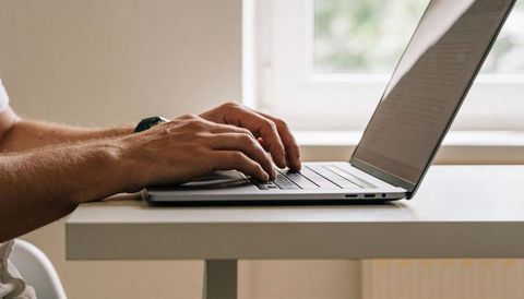 Man typing on laptop at minimal home desk showing hands and forearms, remote work focus