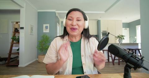 Mature woman podcasting from home studio wearing headphones speaking into microphone