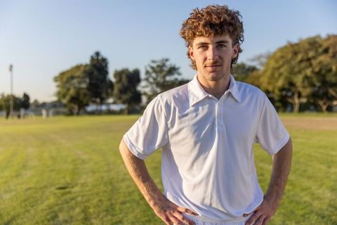 Confident young athlete standing on sunlit grass field wearing white polo and shorts