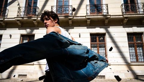 Young male model swinging denim jacket on sunlit urban street, dynamic motion portrait