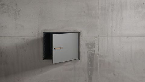 Recessed metal access hatch swinging open in concrete wall with wooden handle and rails