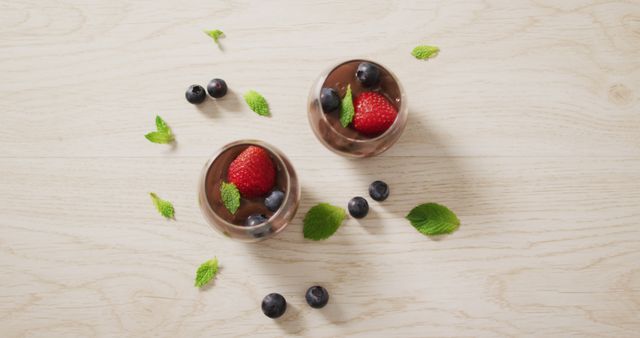 Delicious chocolate mousse topped with strawberries, blueberries and garnished with fresh mint leaves on wooden background. Ideal for use in marketing materials, food blogs, restaurant menus, or recipe books. Perfect for promoting gourmet desserts, culinary presentations, or showcasing elegant and sophisticated sweet treats.
