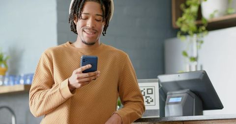 Young African American Man Using Smartphone at Cafe Counter with QR Code, POS and Headphones