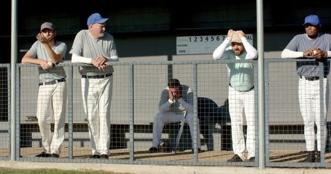 Disappointed baseball teammates leaning on dugout fence with player holding head in hands