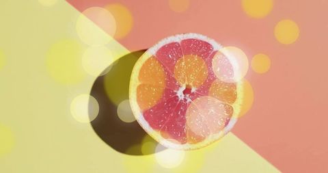 Grapefruit half casting shadow on diagonal pastel background with warm bokeh lights