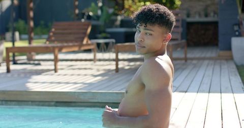 Young man relaxing in backyard pool beside wooden deck and lounge chairs on sunny day