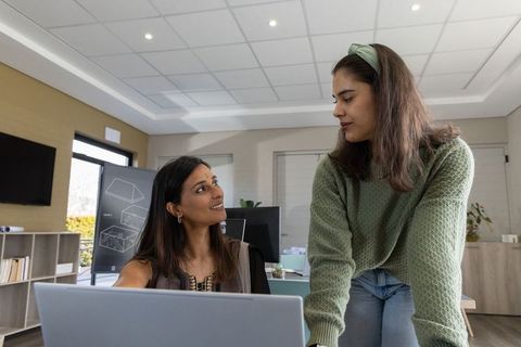 Multiethnic coworkers collaborating over laptop and whiteboard in modern office workspace