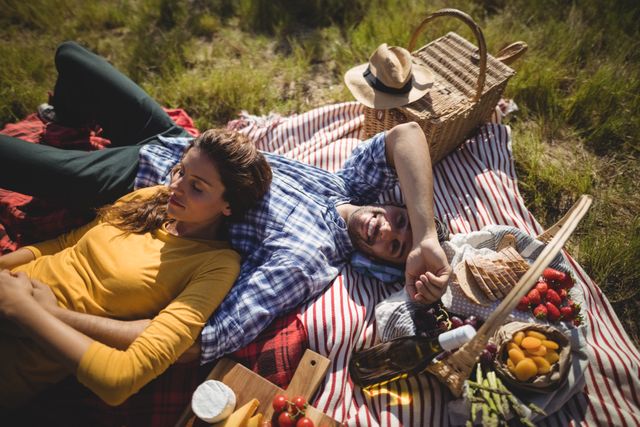 Young couple enjoying a relaxing picnic in an olive farm, lying on a blanket with a basket of food and wine. Ideal for use in advertisements for outdoor activities, romantic getaways, or lifestyle blogs focusing on nature and leisure.