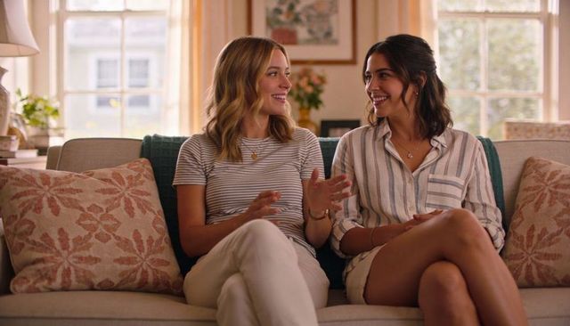 Two women chatting on cozy living room sofa wearing striped shirts smiling casual home