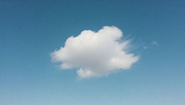 Single cumulus cloud drifting over clear blue sky minimalist calm background
