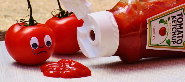 This conceptual image shows a tomato with sad cartoon eyes staring at a ketchup spill from a bottle. The image can be used in creative projects, advertisements, social media content, or blogs to depict humorous anecdotes or concepts related to food, emotions, or funny situations. The light-hearted and playful imagery makes it perfect for creative marketing campaigns.