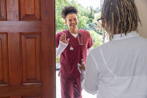 Smiling nurse greeting african american senior woman at home doorway during care visit
