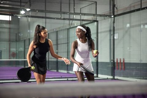 Diverse female padel partners training on indoor purple court holding rackets and balls