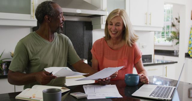 Happy diverse senior couple using laptop computer and paying bills in kitchen. staying at home in isolation during quarantine lockdown.