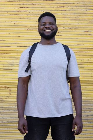 Smiling african american man wearing backpack standing in front of yellow shutter