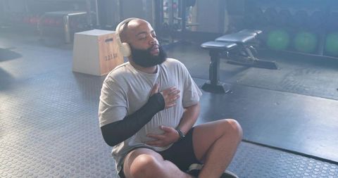 Athlete sitting on gym floor practicing deep breathing wearing headphones and sleeve