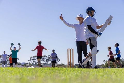 Umpire signaling while batsman holding bat and diverse teammates celebrating in sunny cricket park
