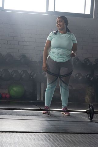Plus-size african american woman preparing to lift barbell in industrial gym, strength