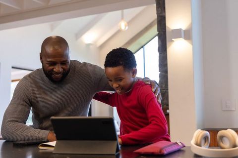 African american father and son sharing tablet at kitchen counter, smiling and learning