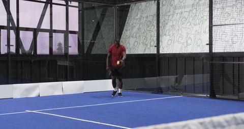Athletic Man Training on Modern Blue Padel Court by Glass Wall