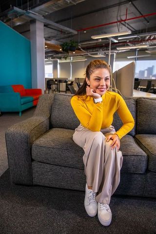 Young woman sitting on gray sofa in modern office lounge checking smartwatch