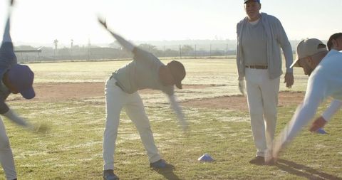 Baseball team stretching with coach on dewy field at sunrise for morning training and teamwork